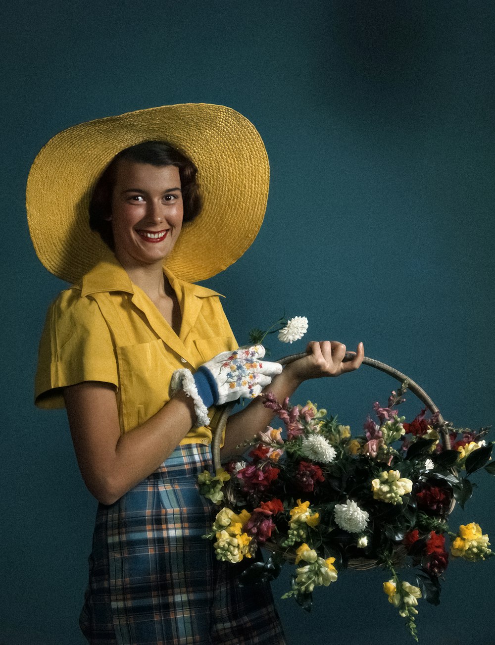 a woman wearing a yellow hat holding a basket of flowers