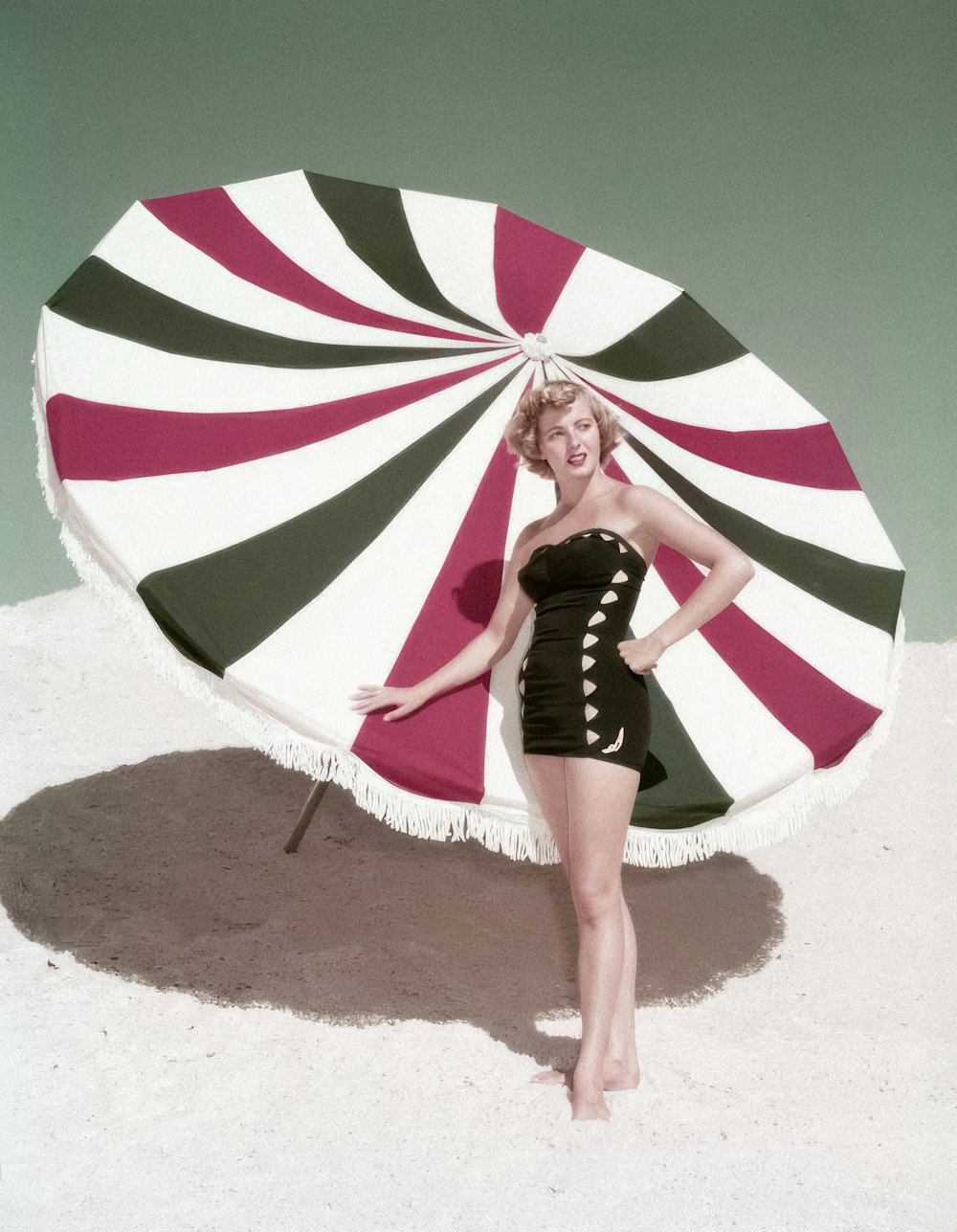 a woman in a bathing suit holding a large striped umbrella