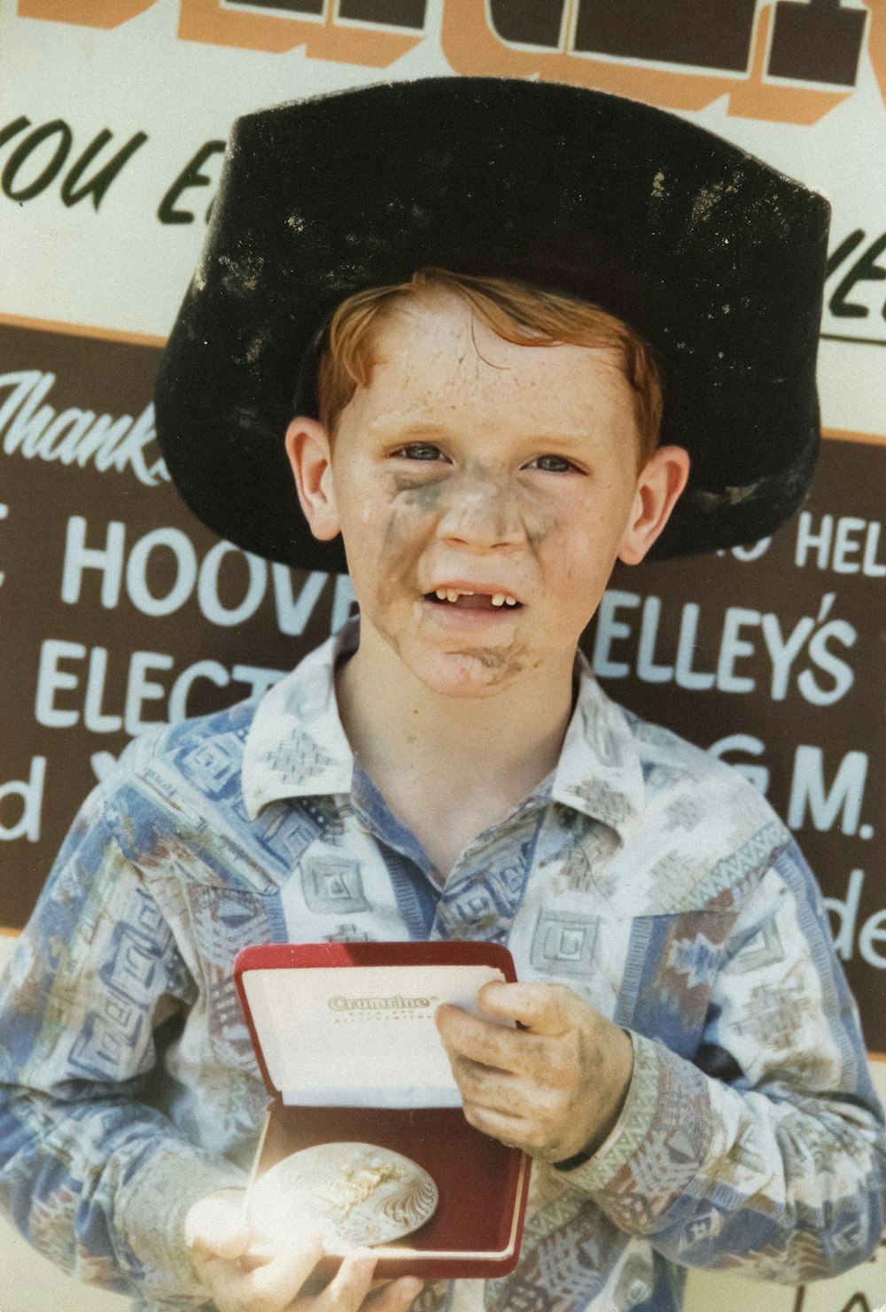 a young boy wearing a black hat and holding a medal