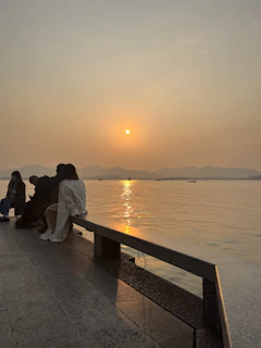 Group of friends sitting by a quiet lake reflecting snowy mountains during the sunset.