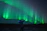 A happy traveler standing under the Northern Lights in Finland, smiling with awe.