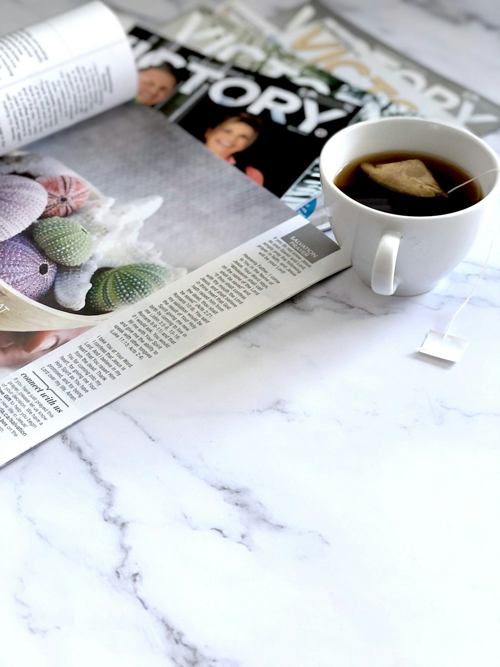 uma xícara de café sentada em cima de uma mesa ao lado de uma revista