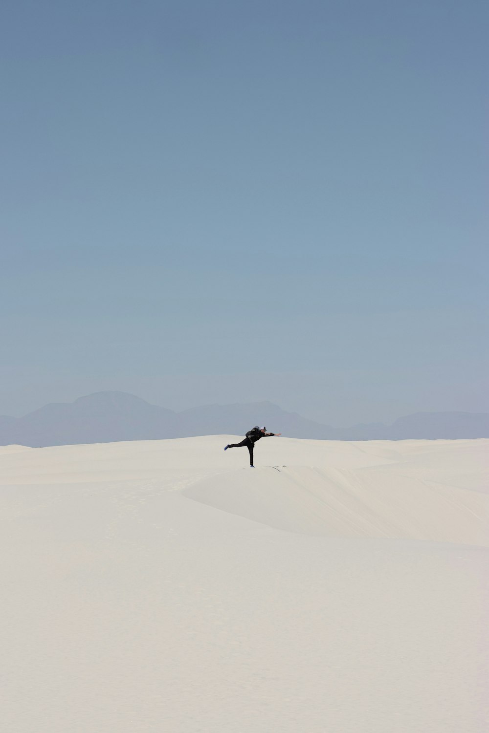 a lone bird flying over a large white desert