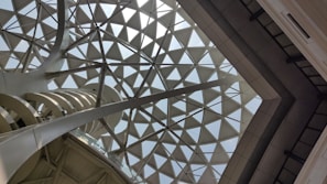 Geometric glass ceiling with triangular panes supported by metal beams, illuminating the space with natural light.