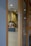 Two people wearing caps and uniforms appear to be working in a contemporary kitchen or cafe setting seen through a wooden-framed glass partition. The lighting is soft with ceiling lights providing a warm tone to the room.