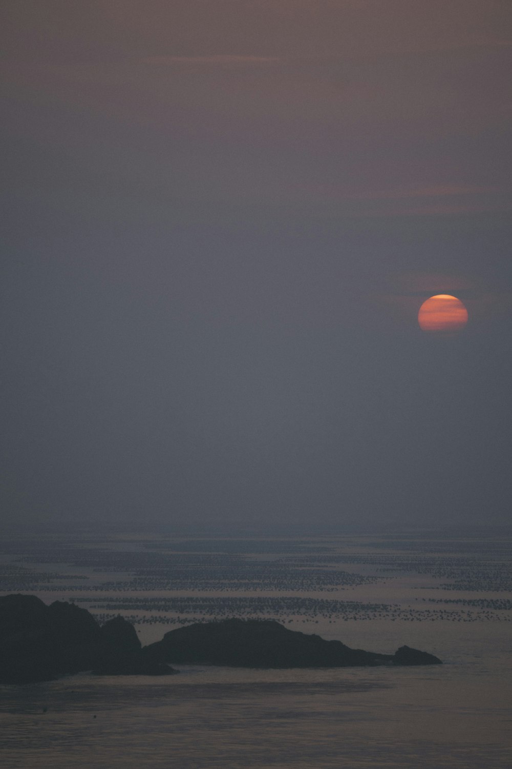 the sun is setting over the ocean with a small island in the foreground