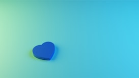 A blue heart shape rests on a gradient background transitioning from light green to turquoise.