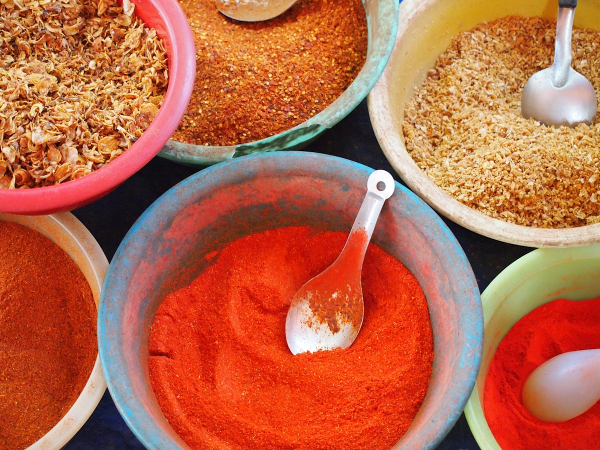 Bowls of taco seasoning spices — chili powder, cumin, paprika, garlic, oregano — laid out on wooden table