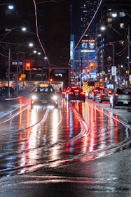 A bustling city street at night with colorful lights reflecting on wet pavement.