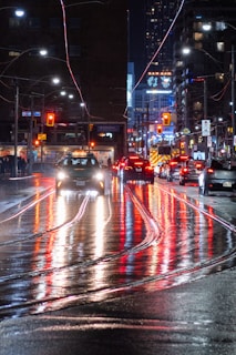 A bustling city street at night with colorful lights reflecting on wet pavement.