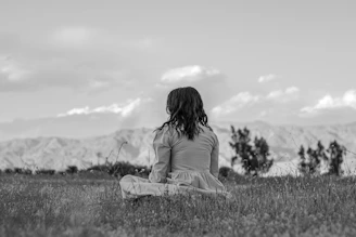 a woman sitting in a field with mountains in the background