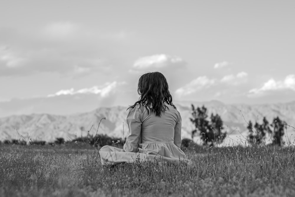 a woman sitting in a field with mountains in the background