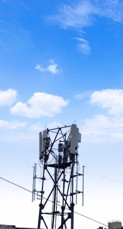 Telecom engineers inspecting a towering cellular mast against a clear blue sky.