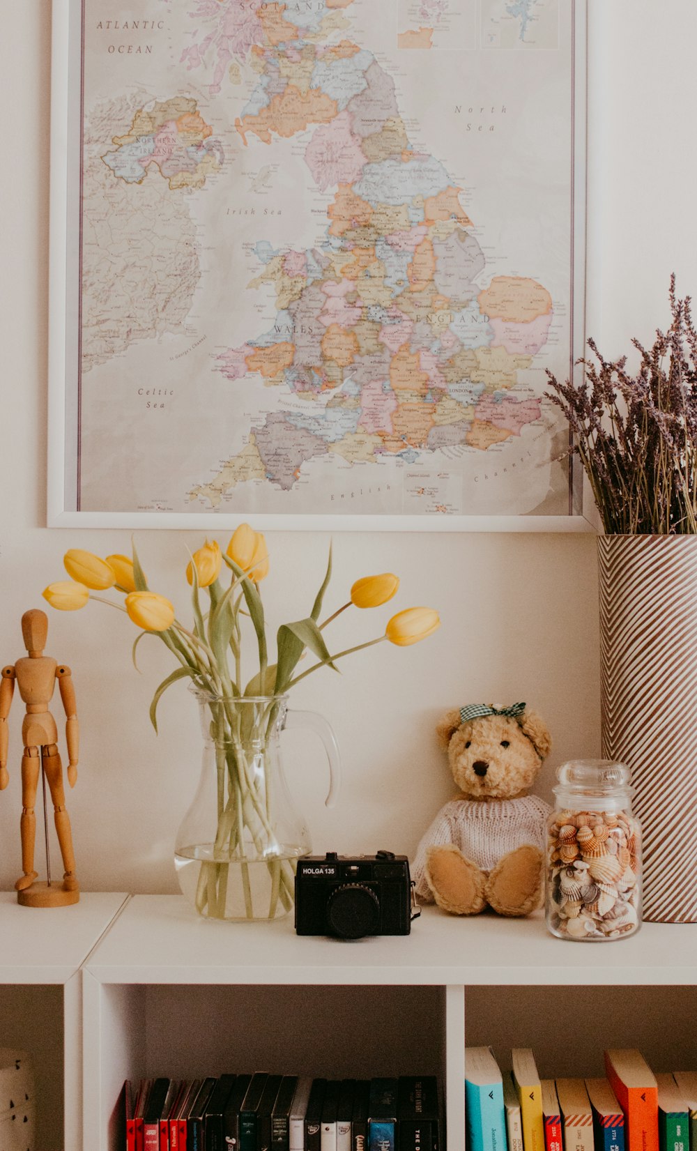 a vase with flowers and a teddy bear on a shelf