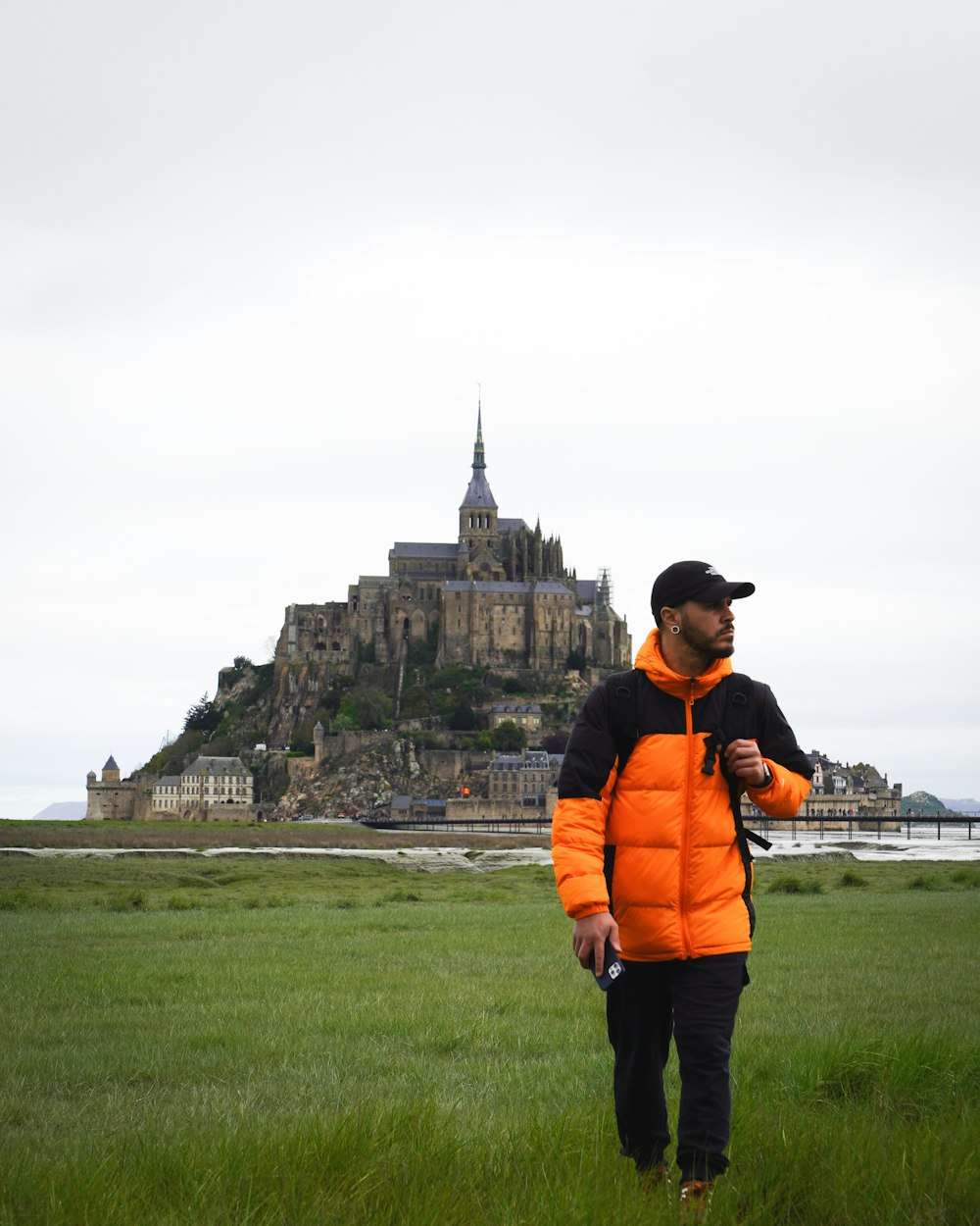a man in an orange jacket standing in a field in front of a castle