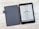 An e-reader with a black cover is open on a textured light-colored surface. The screen displays information in a foreign language with an illustration of a boat under the title 'KON-TIKI-3.' A series of specifications and icons is listed below.