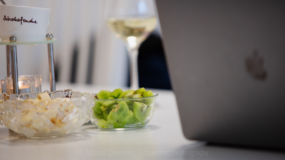 a glass of wine next to a bowl of food and a laptop