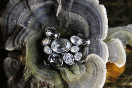 An arrangement of multiple clear gemstones of varying shapes and sizes set in a metallic frame, placed on a textured surface resembling a natural mineral formation with concentric patterns.