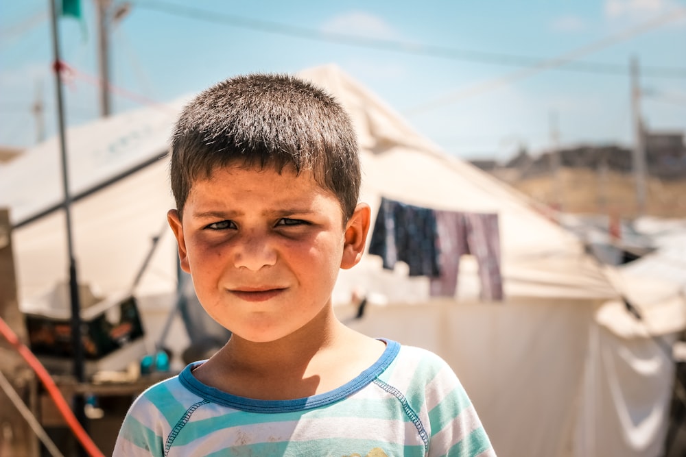 a young boy standing in front of a tent