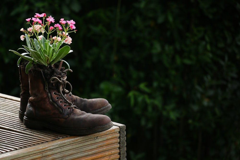 a pair of boots with flowers in them sitting on a wooden bench