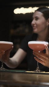 Close-up of hands holding elegant cocktails with a blurred festival stage in the background.