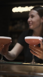 Close-up of hands holding elegant cocktails with a blurred festival stage in the background.