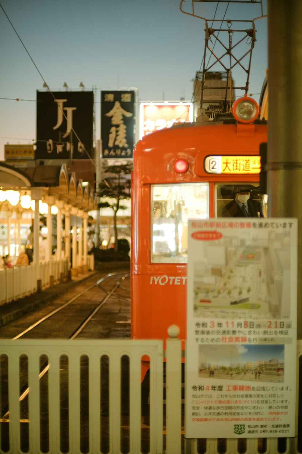 a red train traveling down train tracks next to a white fence