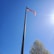 Hands carefully assembling a flagpole outdoors with sunlight filtering through trees.
