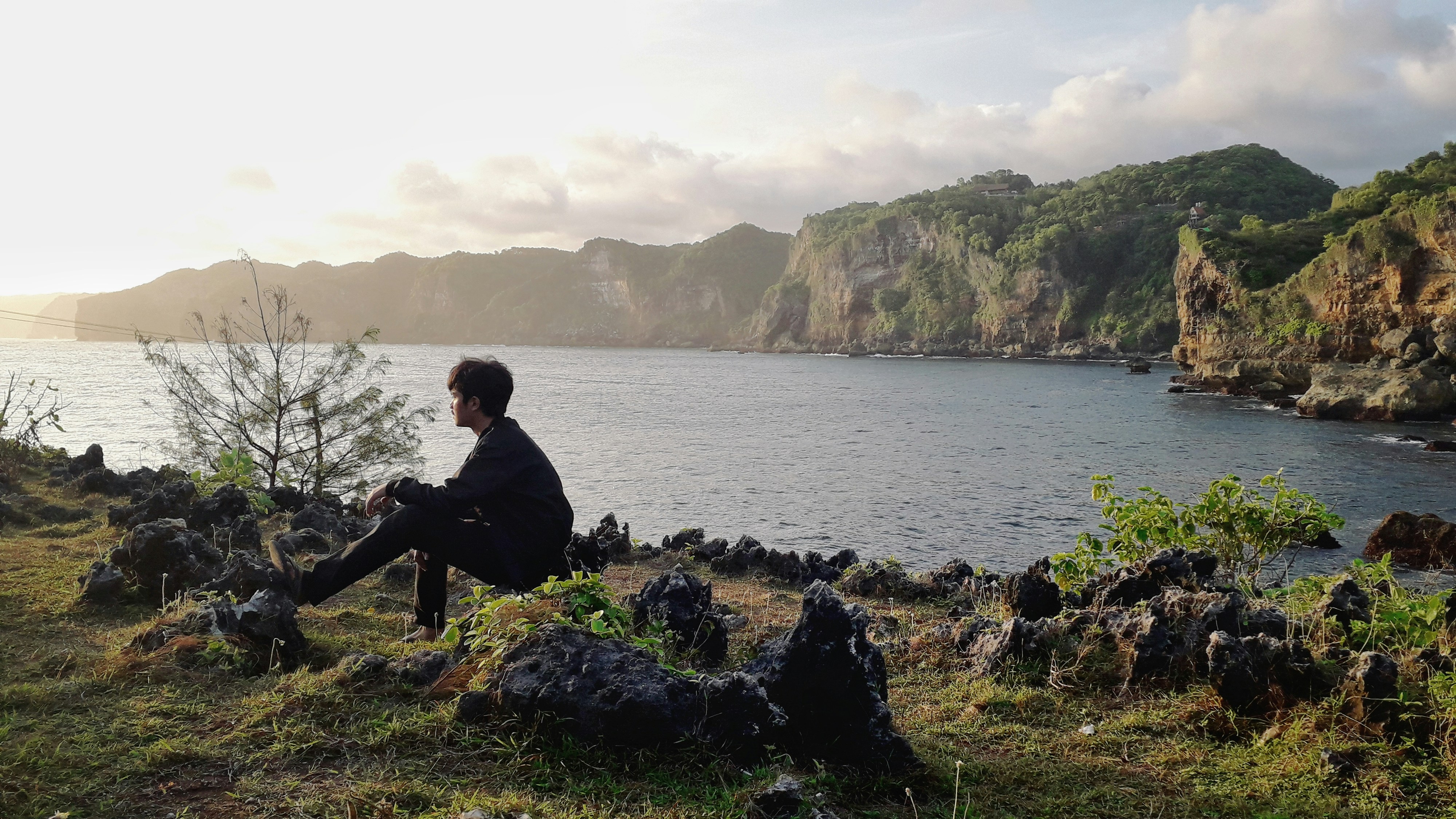 a person sitting on a hill overlooking a body of water, Golden Hour at Kesirat Beach, Gunungkidul, Special Region of Yogyakarta