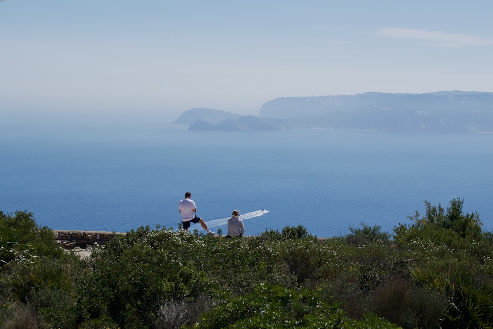 two people carrying a surfboard on a hill overlooking the ocean