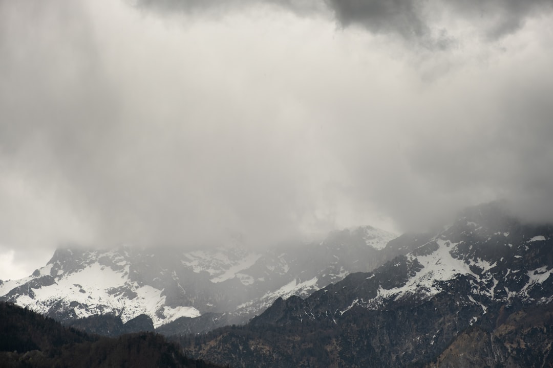 a mountain range covered in snow under a cloudy sky, the weather is fine today