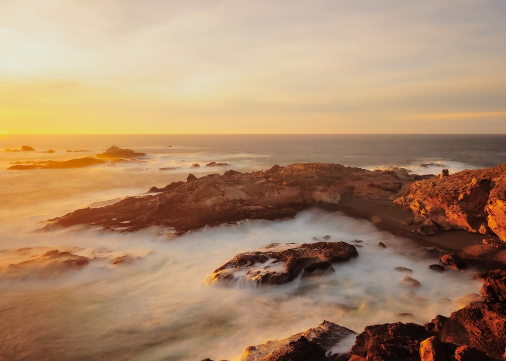 the sun is setting over a rocky beach