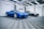 Two luxury sports cars are parked in an elegant, modern showroom with a checkered floor and overhead lighting. The car in the foreground is a vibrant blue with sleek curves, while the car in the background has a metallic silver finish.