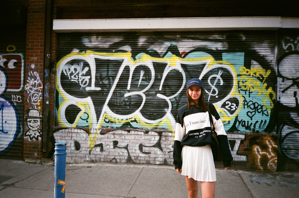 a woman standing in front of a graffiti covered wall