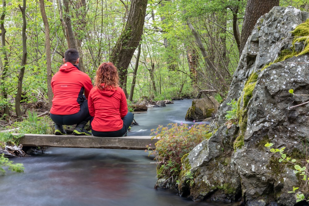 two people sitting on a bridge over a stream