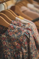 Brightly patterned dresses and pants hanging side by side on a rustic wooden hanger.