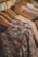 Several wooden hangers hold a variety of floral-patterned clothing items, with the focus on a richly patterned dress or blouse in the foreground. The hanging garments display a mixture of colorful flowers in shades of red, orange, and blue on darker backgrounds.