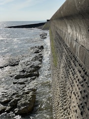 A sturdy seawall along a calm waterfront with a custom-colored finish reflecting sunlight.