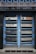 A double door painted in blue with metallic horizontal bars across each section. Above the doors, a row of vertical metal bars is attached to an overhanging section. The doors and the structure surrounding them exhibit a combination of industrial and modern design.