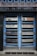 A double door painted in blue with metallic horizontal bars across each section. Above the doors, a row of vertical metal bars is attached to an overhanging section. The doors and the structure surrounding them exhibit a combination of industrial and modern design.