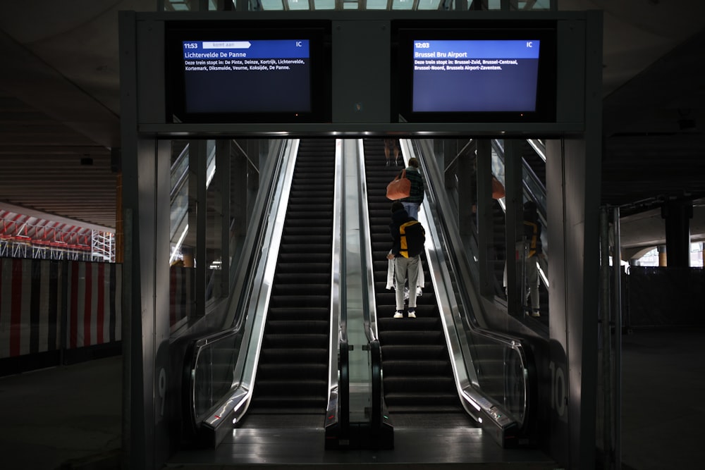a person riding an escalator with two monitors above them