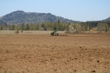 A tractor preparing a vast field under a clear blue sky.