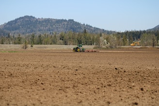 A farmer preparing soil in a lush green field under a clear blue sky.