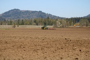 A tractor preparing a vast field under a clear blue sky.