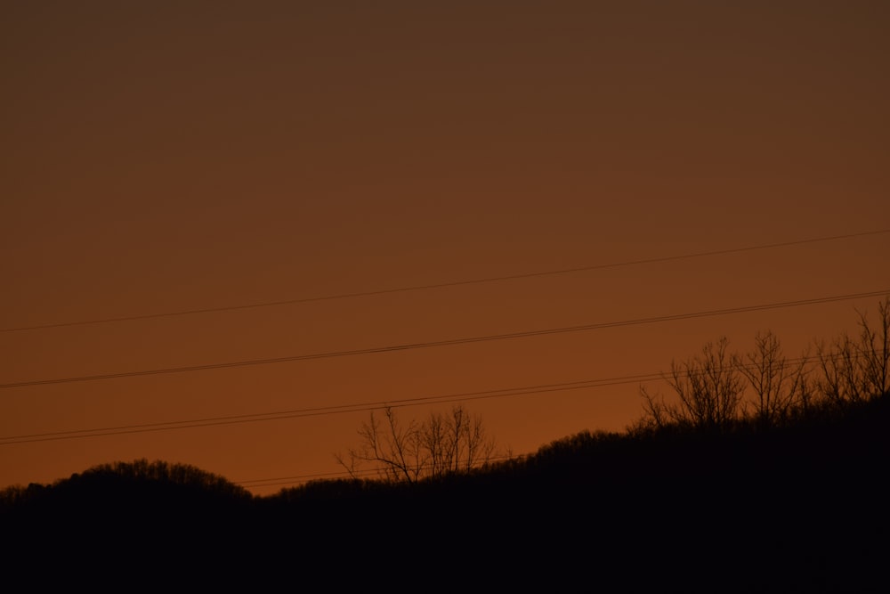 a silhouette of a hill with power lines in the distance