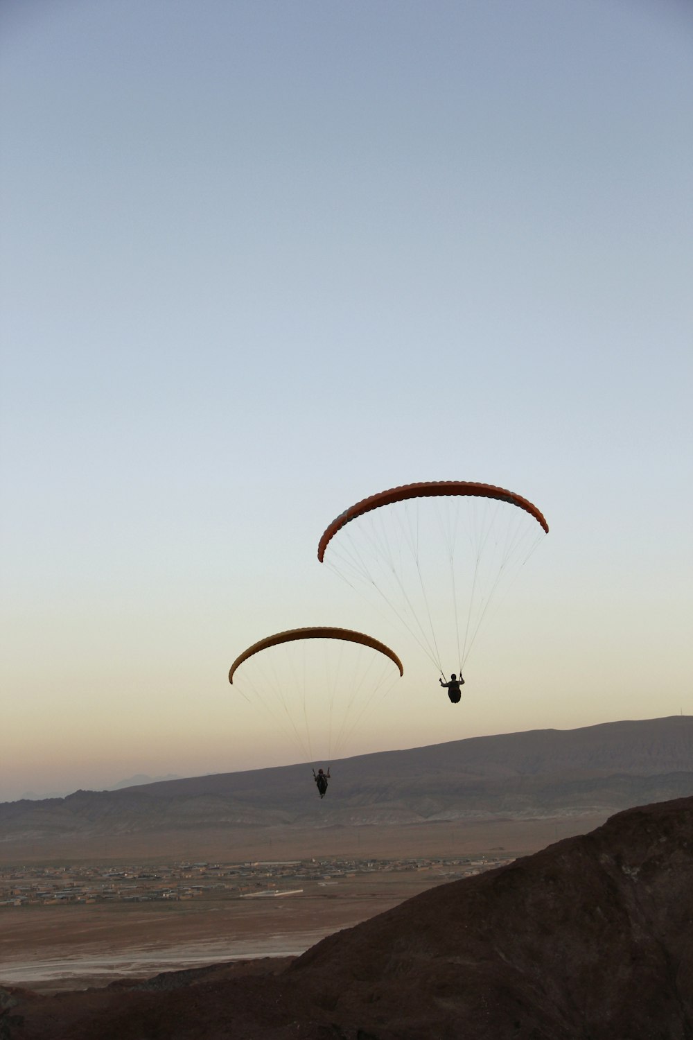 two parasailers in the air over a desert landscape