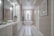 A spacious and elegant bathroom features a long white vanity with a large mirror and modern lighting. The room has a bathtub situated under a window with sheer curtains, a decorative plant, and a chandelier overhead. Neutral tones and clean lines create a sophisticated and serene atmosphere.