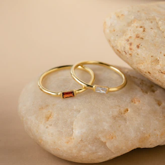 Minimalist rings arranged on a muted sand-colored surface, catching soft natural light.