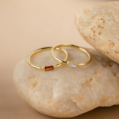 Minimalist rings arranged on a muted sand-colored surface, catching soft natural light.