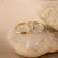 Elegant gemstone ring resting on a smooth cream fabric with soft gold accents in the background.